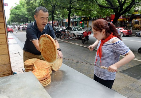 阿卜杜拉的女儿阿依谢姆正在餐厅里帮助买馕的顾客装袋，她平时放学后也会帮助父亲干点力所能及的活。（6月21日摄）